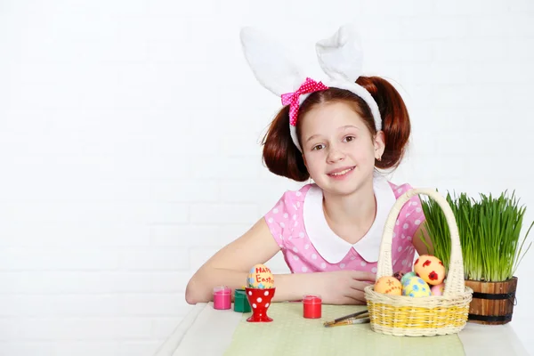 Leuk meisje siert paaseieren, op lichte achtergrond — Stockfoto