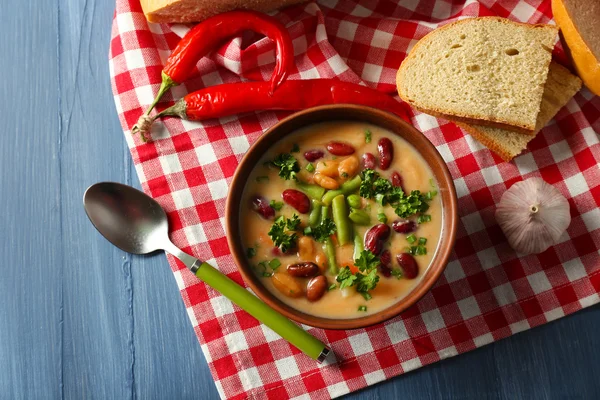 木製のテーブルの色の背景上のナプキンに新鮮な食パンをボウルに豆のスープ — ストック写真