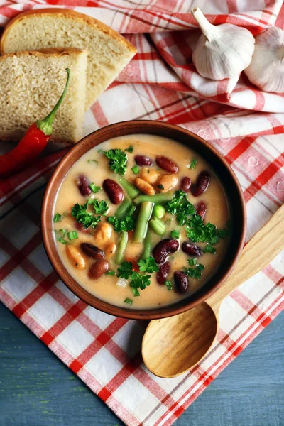 Bean soup in bowl with fresh sliced bread on napkin, on wooden table background — Stock Photo, Image