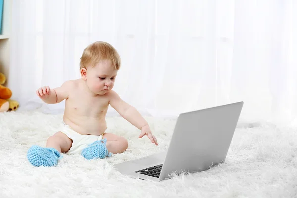 Bonito menino sentado com laptop no tapete, no fundo de luz — Fotografia de Stock