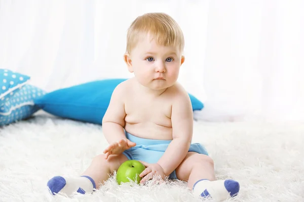 Söt baby pojke med grönt äpple på mattan, på ljus bakgrund — Stockfoto