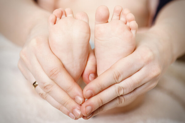 Newborn baby feet on female hands, close-up