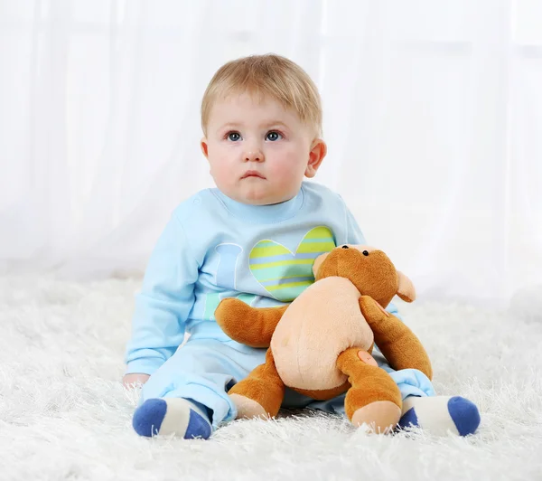 Bonito menino com ursinho de pelúcia no tapete, no fundo claro — Fotografia de Stock