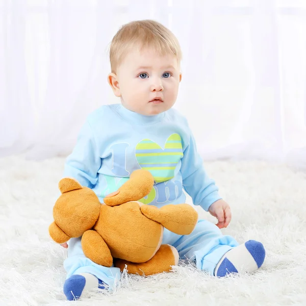 Carino bambino con orsacchiotto su tappeto, su sfondo chiaro — Foto Stock