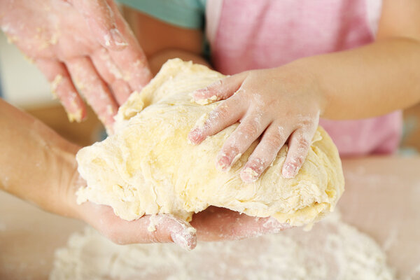 Little girl preparing cookies with mother in kitchen, close-up