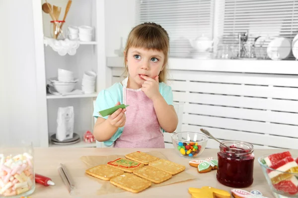 Little girl decorating prepared cookies in kitchen at home — Stock Photo, Image