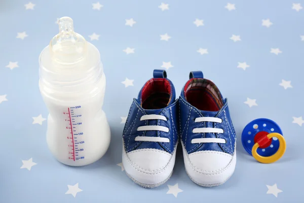 Chaussures bébé avec mamelon et biberon de lait sur fond bleu — Photo