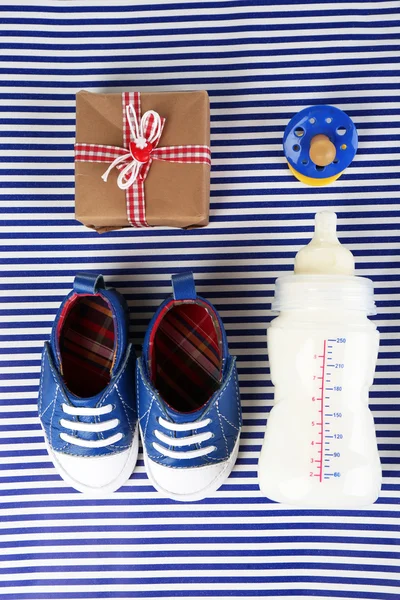 Babyschuhe mit Geschenk und Flasche Milch auf blauem Hintergrund — Stockfoto