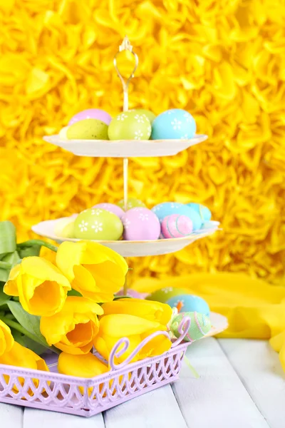 Пасхальные яйца на вазе и тюльпаны на столе на желтом фоне — стоковое фото