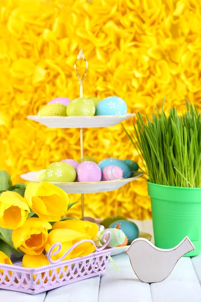 Easter eggs on vase and tulips on table on yellow background — Stock Photo, Image