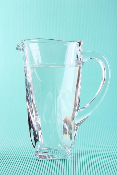 Glass pitcher of water on blue background — Stock Photo, Image