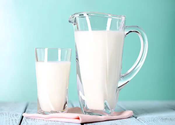 Pitcher and glass of milk on wooden table on blue background — Stock Photo, Image