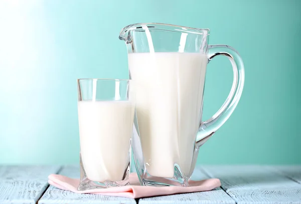 Brocca e bicchiere di latte su tavolo di legno su sfondo blu — Foto Stock