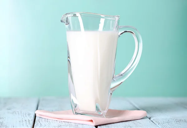 Brocca di latte su tavolo di legno su sfondo blu — Foto Stock