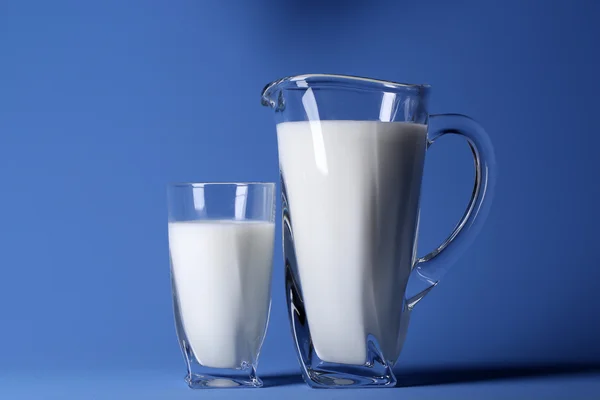 Pitcher and glass of milk on blue background — Stock Photo, Image