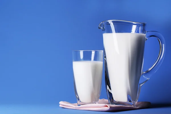 Krug und Glas Milch auf blauem Hintergrund — Stockfoto