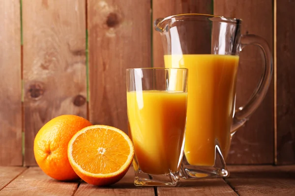 Bicchiere e brocca di succo d'arancia su tavolo di legno su sfondo di legno — Foto Stock