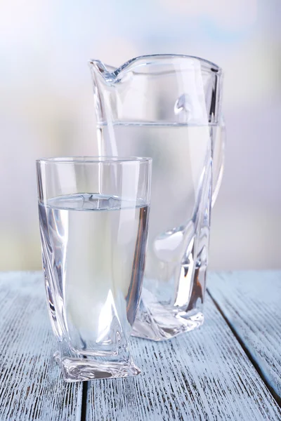 Glass pitcher and glass of water on wooden table on bright background — Stock Photo, Image