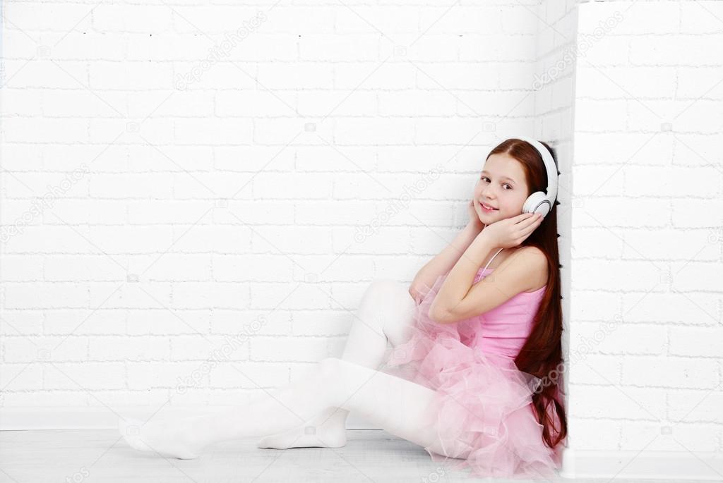 Beautiful little ballerina with headphones on  white bricks wall background