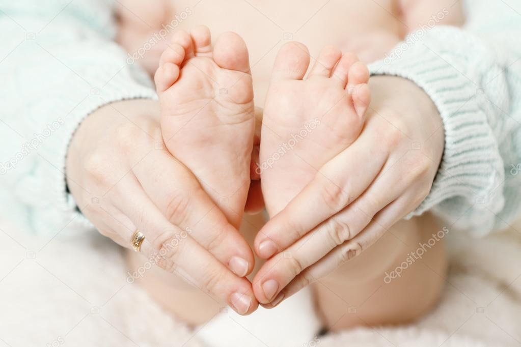 Newborn baby feet on female hands, close-up