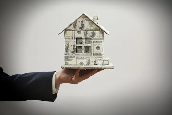 Model of house made of money in male hand on gray background — Stock Photo, Image