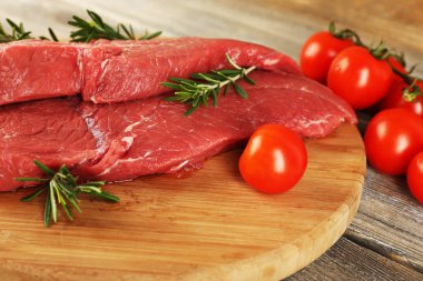 Biberiye ve domates ahşap arka plan üzerinde kesme tahtası üzerinde ham sığır eti biftek