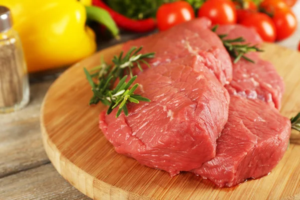 Raw beef steak on cutting board with vegetables and greens on wooden background — Stock Photo, Image