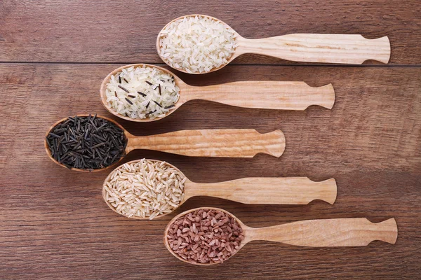 Different kinds of rice in spoons on wooden background — Stock Photo, Image