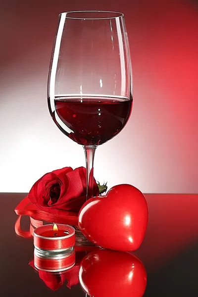 Compoziție cu vin roșu în sticlă, trandafir roșu și inimă decorativă pe fundal colorat — Fotografie, imagine de stoc