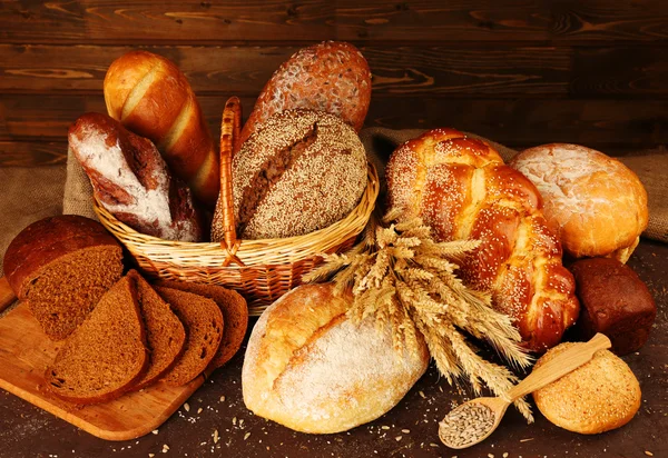 Different bread with ears in basket on wooden background — Stock Photo, Image