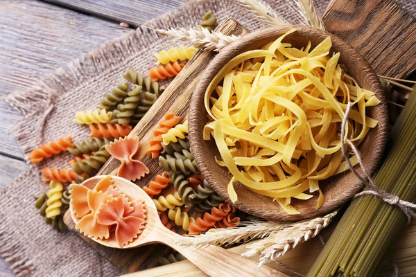 Verschillende soorten pasta op zak op houten achtergrond — Stockfoto