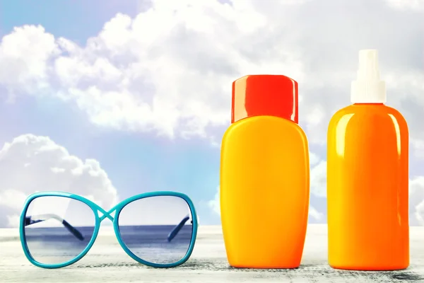 Botellas con crema bronceadora con gafas de sol sobre mesa aislada en blanco —  Fotos de Stock