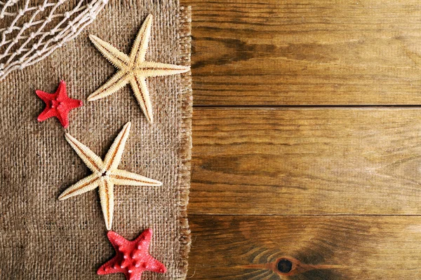 Морские звезды на мешковине на деревянном фоне — стоковое фото