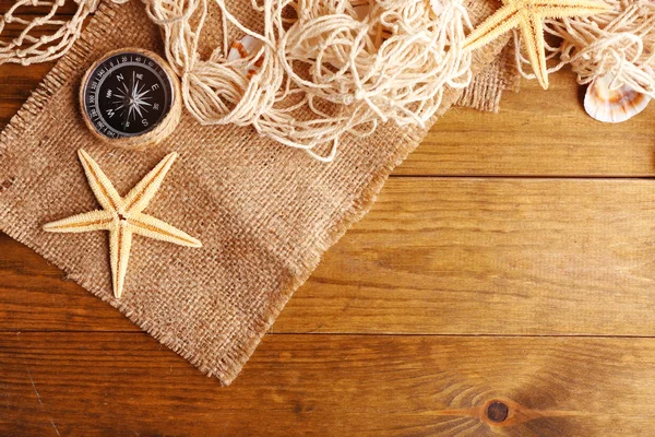 Sea stars with compass on sackcloth on wooden background — Stock Photo, Image