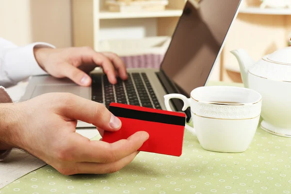 Man holding credit card and working on laptop on home interior background — Stock Photo, Image