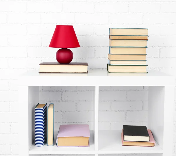 Estante de madera con libros y lámpara sobre fondo de pared de ladrillo — Foto de Stock