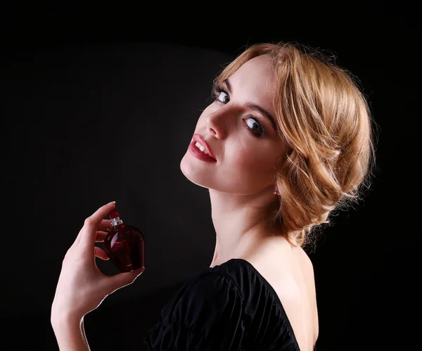 Hermosa joven con botella de perfume sobre fondo negro —  Fotos de Stock