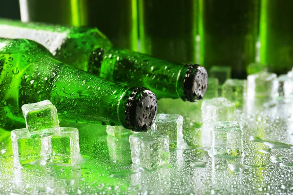 Botellas de vidrio de cerveza con cubitos de hielo sobre mesa húmeda, primer plano — Foto de Stock