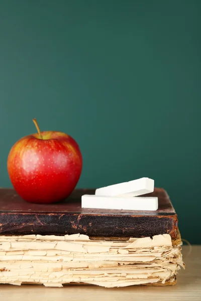 Old books, apple and chalk on blackboard background — Stock Photo, Image