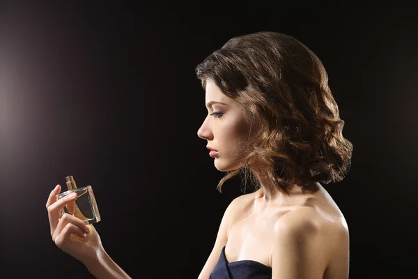 Beautiful woman with perfume bottle on dark background — Stock Photo, Image