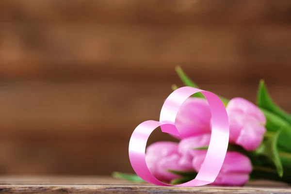 Bei tulipani rosa con cuore decorativo su sfondo di legno — Foto Stock