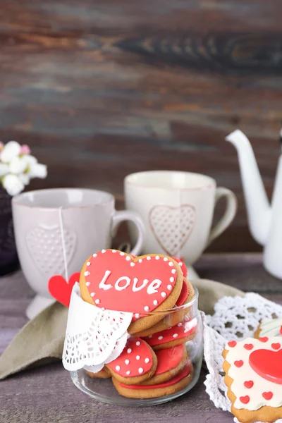 Herzförmige Plätzchen zum Valentinstag, Teekanne und Tassen auf farbigem Holzhintergrund — Stockfoto