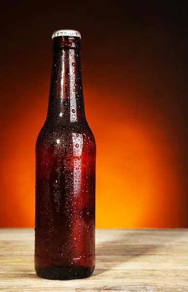 Glass bottle of beer on wooden table on dark color background — Stock Photo, Image