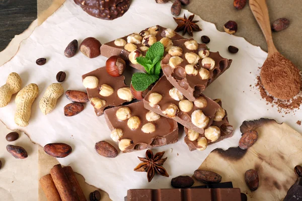 Chocolate with nuts, spices and mint on paper, closeup — Stock Photo, Image