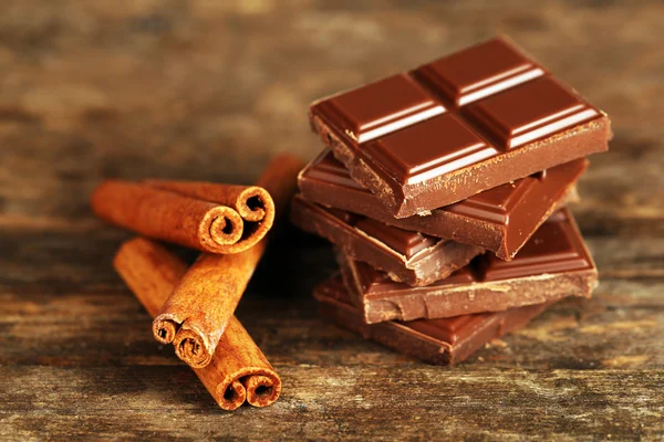 Stukken van chocolade met kaneelstokjes op houten achtergrond — Stockfoto