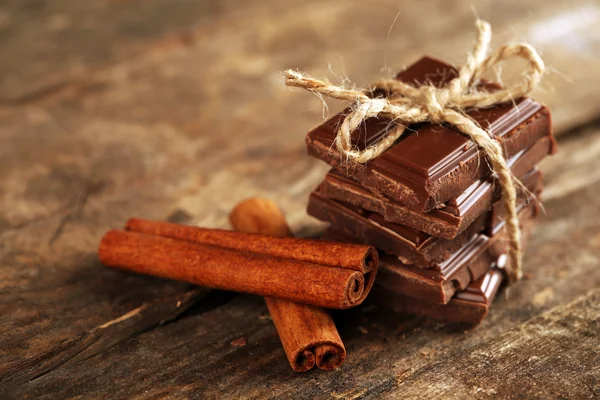Morceaux de chocolat avec bâtonnets de cannelle sur fond en bois — Photo
