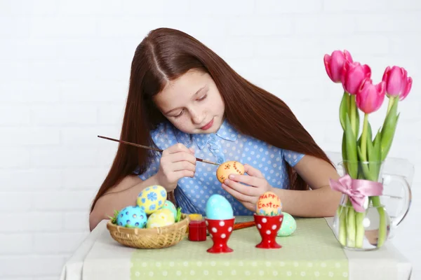 Cute girl decorates Easter eggs, on light background — Stock Photo, Image