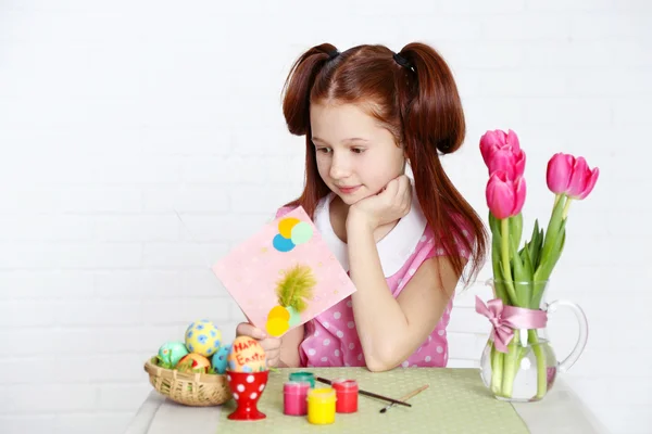 Cute girl  with greeting card and decorated Easter eggs, on light background — Stock Photo, Image