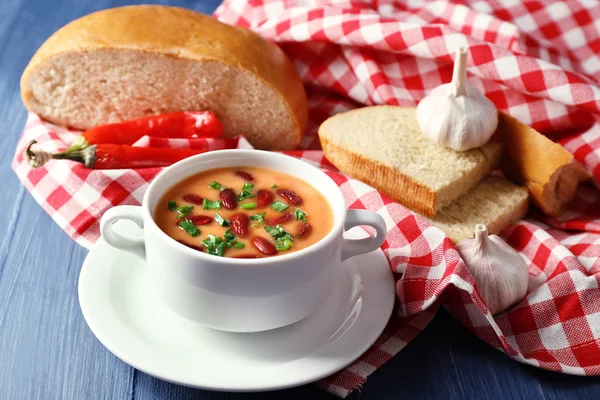 Sopa de feijão na tigela com pão fresco fatiado no guardanapo, na cor de fundo de mesa de madeira — Fotografia de Stock