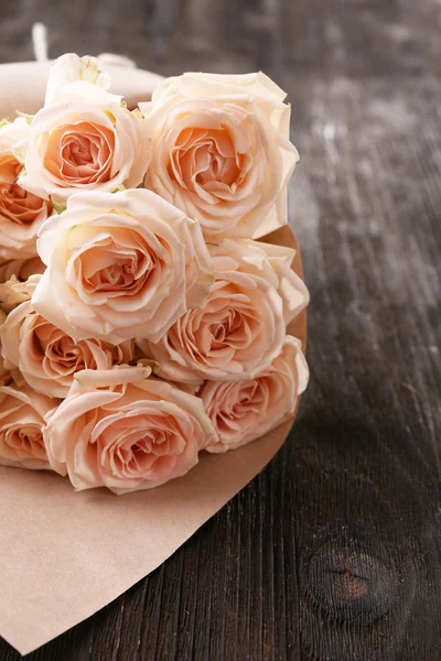 Букет красивых свежих роз, завернутых в бумагу на деревянном фоне — стоковое фото